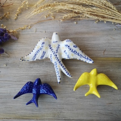 Três pássaros de cerâmica coloridos em madeira com ramos secos