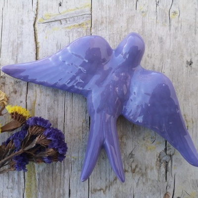 Figura decorativa de cerâmica roxa em forma de pássaro com asas abertas