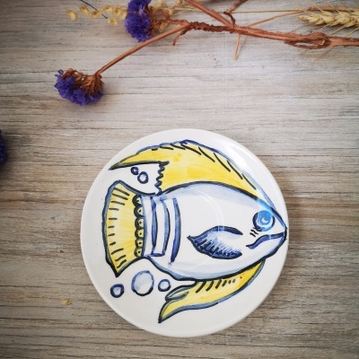Prato decorativo de cerâmica com desenho de peixe amarelo e azul sobre mesa de madeira