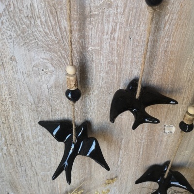 Decoração de pássaros de cerâmica preta pendurados em cordas com contas de madeira sobre fundo de madeira clara