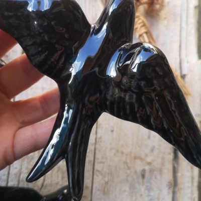 Escultura brilhante de pássaro preto sendo segurada por uma mão sobre fundo de madeira clara