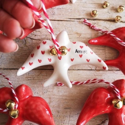 Enfeites de estrela de cerâmica vermelha e branca com sinos e cordões colocados sobre mesa de madeira clara