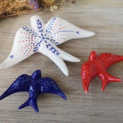 Três pássaros decorativos de cerâmica coloridos sobre superfície de madeira.