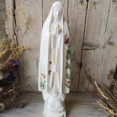 Estatueta branca de Nossa Senhora com pintura floral sobre fundo de madeira rústica