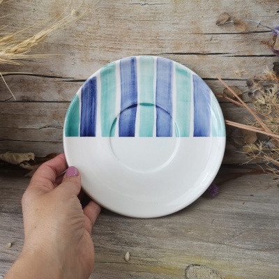 Prato cerâmico azul, verde e branco com mão a segurá-lo em madeira com flores secas