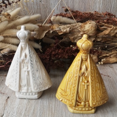 Duas estatuetas religiosas de cerâmica branca e amarela sobre madeira clara