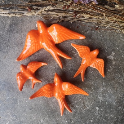 Quatro pássaros decorativos de cerâmica laranja sobre superfície cinzenta com ramo seco ao fundo