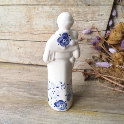 Figura decorativa cerâmica branca com pinturas florais azuis e vegetação seca ao lado