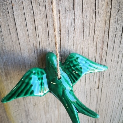 Ornamento de pássaro de cerâmica verde pendurado em corda sobre fundo de madeira