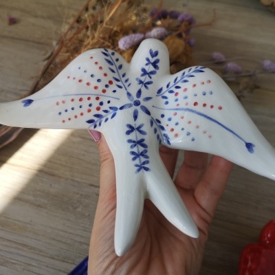 Ornamento de cerâmica em forma de pássaro branco com padrões azuis e vermelhos