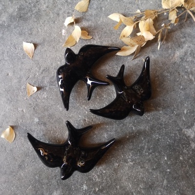 Três figuretas de aves pretas em cerâmica com folhas secas ao redor