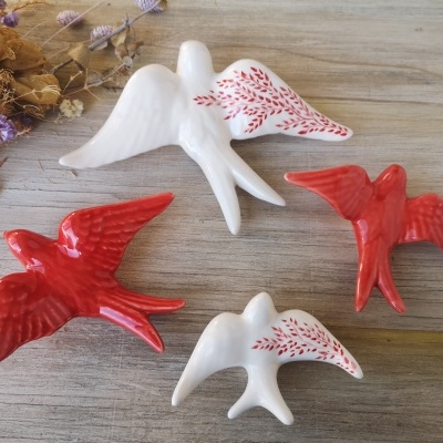 Figuras decorativas de pássaros em cerâmica vermelha e branca sobre madeira clara