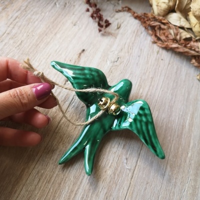 Ornamento pássaro cerâmica verde com corda e sinos dourados sobre superfície de madeira
