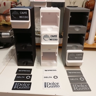 Suportes de cápsulas de café de plástico em preto, branco e cinza com etiquetas para diferentes marcas na bancada da cozinha.