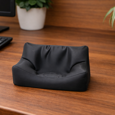 Mini sofá preto numa mesa de madeira com teclado, monitor e plantas ao fundo