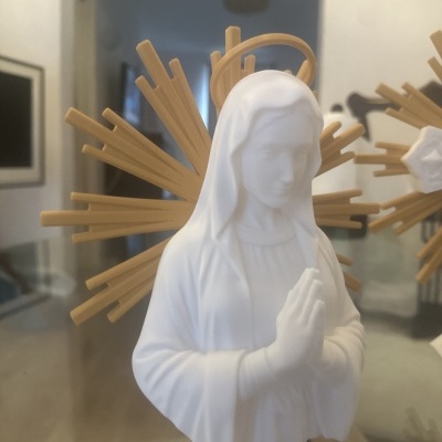 Estátua branca de Nossa Senhora com halo dourado e mãos em oração