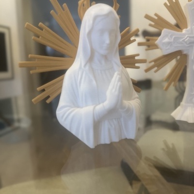 Estátua branca de Nossa Senhora com halo dourado no fundo