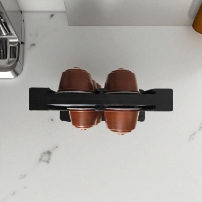 Suporte preto com cápsulas de café castanhas sobre bancada branca e máquina de café inox