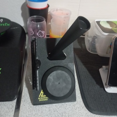 Base preta de suporte com várias peças em superfície branca e copos coloridos ao fundo.