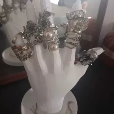 Mão branca exibindo vários anéis prateados com pedras e pérolas