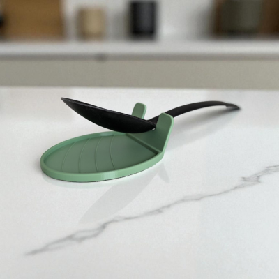 Descanso de colher verde em silicone com colher preta num balcão de cozinha.