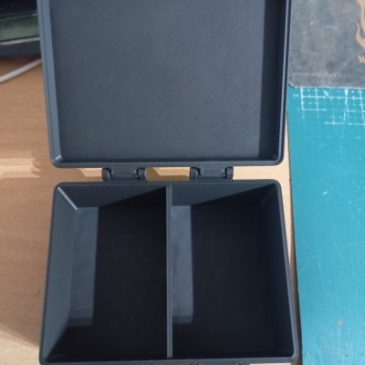 Caixa organizadora preta com divisórias e fechos vermelhos sobre mesa de madeira