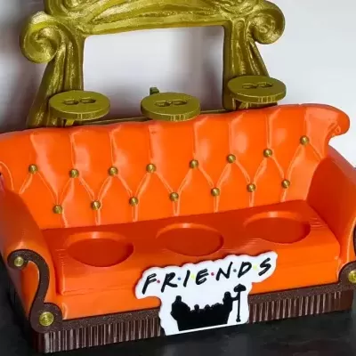 Cofre em forma de sofá alaranjado com detalhes dourados e placa com texto FRIENDS