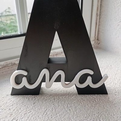 Figura decorativa letra A preta com palavra ana em branco cursivo