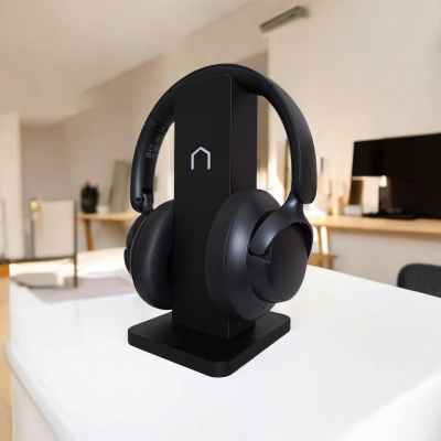 Auscultadores sem fios pretos num suporte preto sobre mesa branca numa sala de estar.