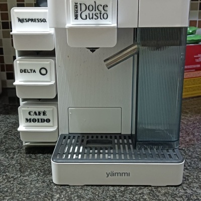 Máquina de café branca Yämmi com etiquetas de diferentes marcas de café numa bancada de cozinha.