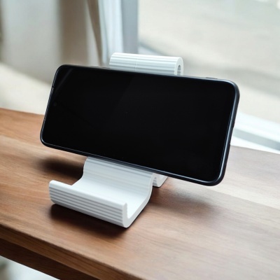 Suporte de telemóvel branco com telemóvel preto na horizontal sobre mesa de madeira