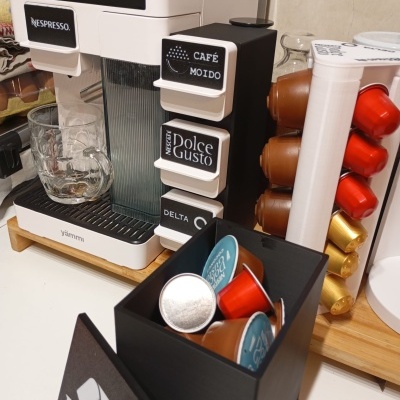 Máquina de café branca com cápsulas coloridas e caixa preta com símbolo de reciclagem