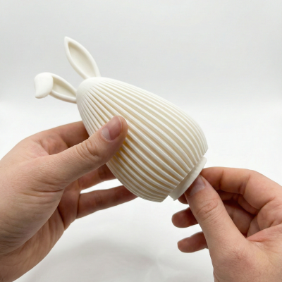 Objeto branco com textura de ranhuras verticais e orelhas de coelho sendo segurado pelas mãos.