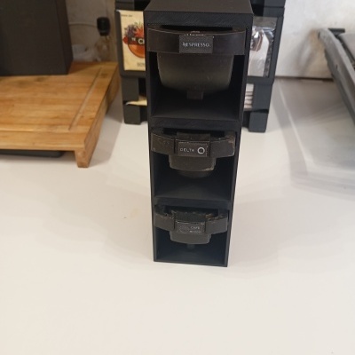 Organizador preto para cápsulas de café em bancada branca com tábua de cortar madeira