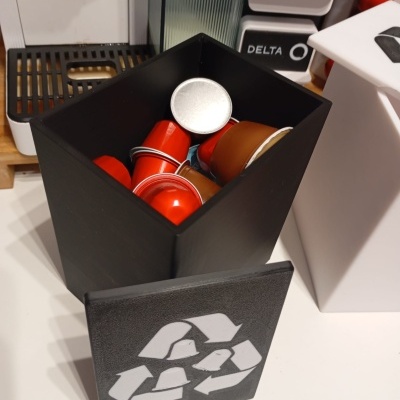 Recipiente para cápsulas de café com símbolos de reciclagem e etiquetas de café ao fundo.