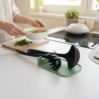 Utensílios de cozinha pretos em base verde sobre bancada branca e pessoa segurando tigela com sopa