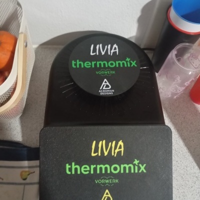 Bases pretas com etiquetas Thermomix sobre bancada de cozinha com cesta de fruta e copos plásticos