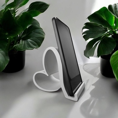 Suporte de smartphone branco em forma de coração com smartphone preto entre plantas verdes em vasos pretos.