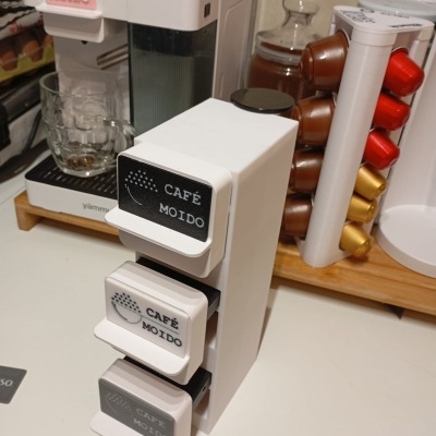 Dispensadores para cápsulas de café brancos com etiquetas CAFÉ MOÍDO e máquina de café ao fundo