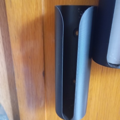 Suporte mural preto para controlo remoto numa porta de madeira.