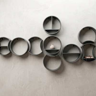 Prateleiras de parede modulares cinzentas em várias formas circulares e meia-lua com objetos decorativos.
