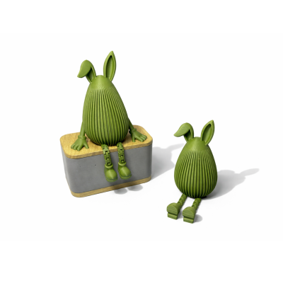 Duas figuras decorativas verdes com orelhas e pernas articuladas, uma sentada num bloco cinza e a outra no chão