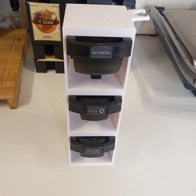 Suporte branco para cápsulas de café com três cápsulas pretas encaixadas e texto NESpresso, DELTA e CAFÉ MOIDO