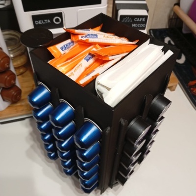 Organizador de cápsulas de café preto com cápsulas azuis e pretas, saquetas de açúcar e guardanapos.