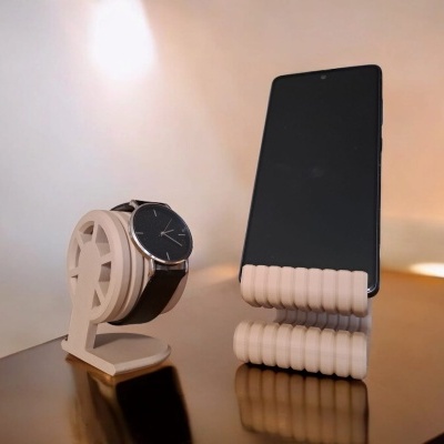 Suportes bege para relógio com alça preta e telemóvel preto numa superfície espelhada