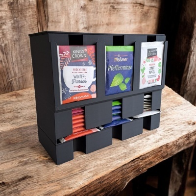 Caixa preta de plástico para organizar saquetas de chá de diferentes sabores e marcas sobre mesa de madeira.