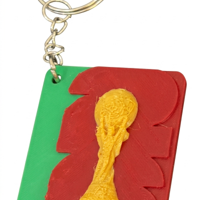 Porta-chaves com réplica da Taça do Mundo FIFA em relevo sobre base verde e vermelho.