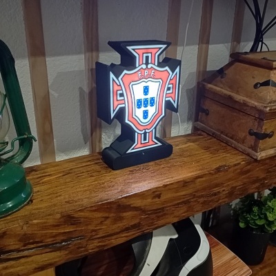 Escultura decorativa de cruz com brasão de Portugal e letras F.P.F.