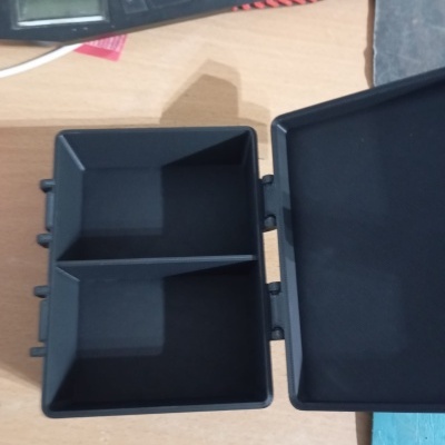 Caixa organizadora plástica preta com tampa aberta sobre mesa de madeira clara