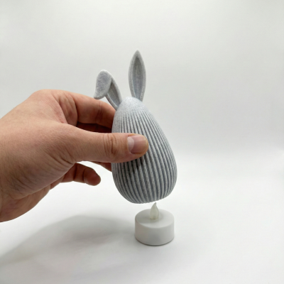 Objeto decorativo coelho cinzento segurado por mão com vela LED branca embaixo